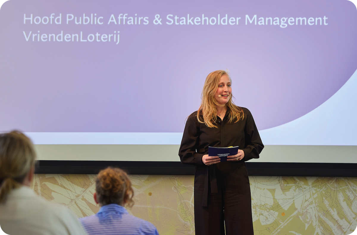 Maaike Zeeuw spreekt tijdens een presentatie, staand voor een scherm waarop haar functie wordt weergegeven: hoofd public affairs en stakeholder management.