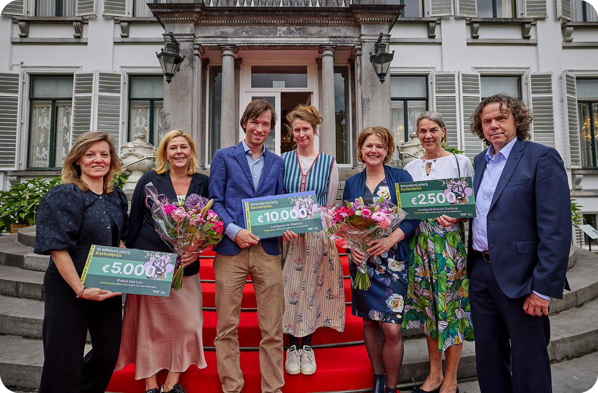 De groep winnaars staat op de trap van Paleis Soestdijk met cheques van €5.000, €10.000 en €2.500.