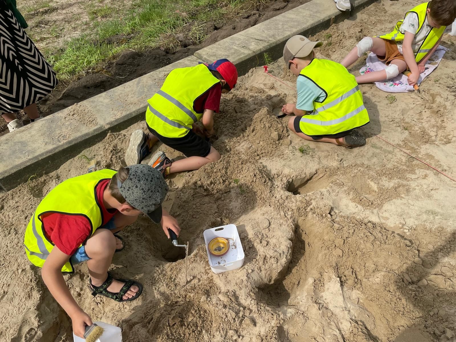 Kinderen dragen gele hesjes en graven in het zand. Kinderen dragen gele hesjes en graven in het zand. Ze gebruiken gereedschap en borstels. Ze doen mee aan een archeologische activiteit buiten.